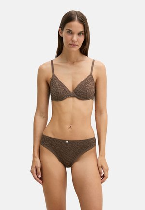 Femme portant un soutien-gorge et un slip marron assortis à motifs, debout devant un fond uni, face à l'avant avec les bras détendus sur les côtés.