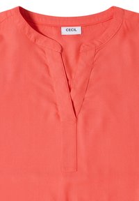 Blouse couleur corail avec encolure en V fendue, sans boutons et étiquette visible de la marque CECIL à l'intérieur du col.