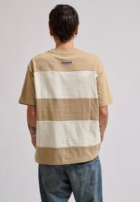 Brun og creme stribet t-shirt med en afslappet pasform, der har korte ærmer og et lille logo i nakken. Lavet af bomuldsmateriale.