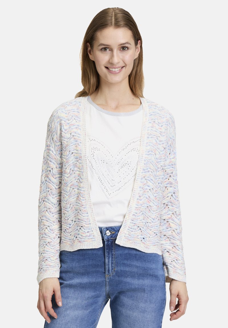 Virkat cardigan med en vågig mönster i pastellfärger, öppen front och långa ärmar. I kombination med en vit skjorta och blå jeans.