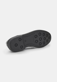 Semelle de chaussure noire avec des motifs de bande de roulement circulaires, présentant des sections en caoutchouc surélevées séparées pour une meilleure adhérence et un bord lisse pour plus de durabilité.