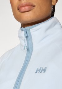 Ανοιχτό γαλάζιο fleece μπουφάν με ψηλό γιακά, κλείσιμο με φερμουάρ και υφή υφάσματος. Διαθέτει ασημένιο λογότυπο «HH» στο μπροστινό μέρος.