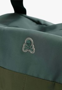 Grüne und olivfarbene Stofftasche mit strukturiertem Oberflächen, einem oberen Griff und einem auffälligen Totenkopf-und-Kreuzfahne-Logo.
