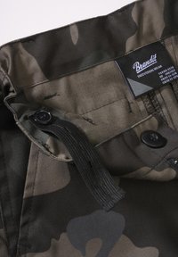 Ceinture de pantalon à motif camouflage avec bouton noir et sangle élastique ajustable, avec étiquette Brandit indiquant la taille adolescent 146/152.