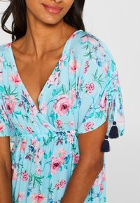 Vestido floral azul claro con rosas rosas y hojas verdes, mangas cortas con acentos de borlas en azul marino y un diseño de escote en V.