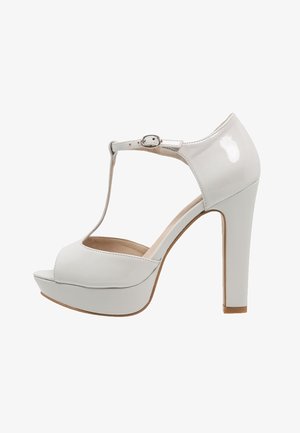 Sandalias de tacón alto de charol blanco con tira en T, punta abierta, suela con plataforma y cierre de hebilla. Textura lisa y acabado brillante.