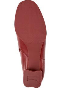 Suela de un zapato de cuero rojo con agarre texturizado y tacón de forma única, visto desde abajo.