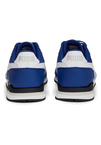 Niebieskie sneakersy Puma mają górę z gładkiego tworzywa sztucznego z białymi skórzanymi akcentami, wyściełany kołnierz i charakterystyczne logo na pięcie. Czarna podeszwa.