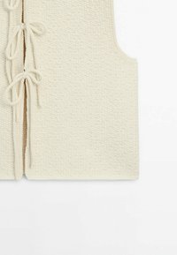 Gilet tricoté couleur crème avec motif texturé et trois nœuds noués sur le devant, sans manches.