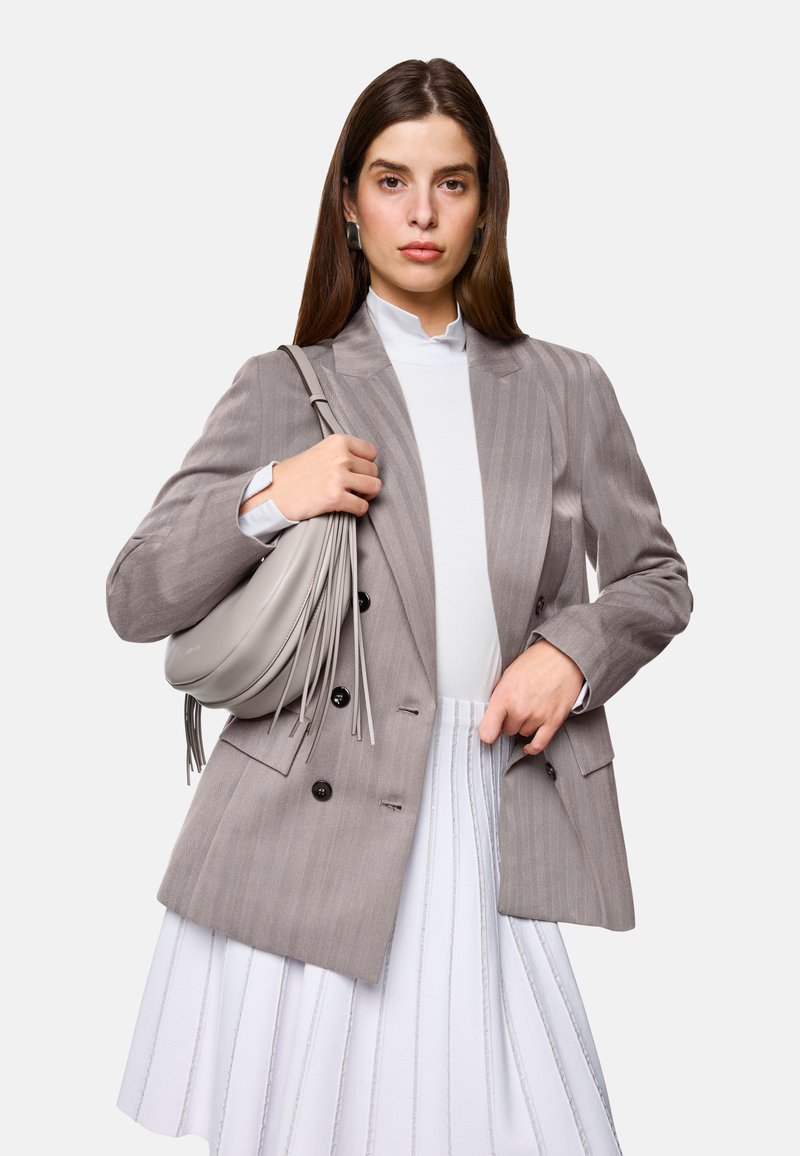 Light gray pinstriped blazer, white high-neck top, and white pleated skirt. Gray bag with fringe detail held in hand. Simple, modern design.
