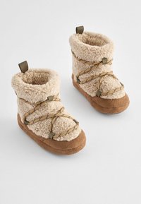 Beige Fleece-Ankle Boots mit einem kuscheligen Textur, versehen mit Kreuzriemen und einer braunen Sohle. Enthält eine Zuglasche für ein einfaches Anziehen.