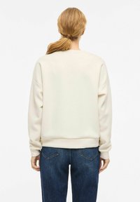 Sweat-shirt couleur crème à coupe décontractée, avec des poignets côtelés et un col rond, associé à un jean en denim bleu foncé.