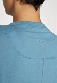 Tela de camiseta atlética azul con textura suave, con cuello redondo y un pequeño logo de Nike en la parte trasera. Detalles visibles de costuras.