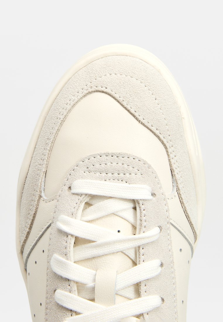 Baskets avec une tige en cuir blanc et en daim gris, bout rond, lacets plats blancs et détails perforés sur les côtés.