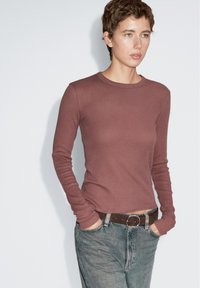 Langärmliges, eng anliegendes Oberteil in einem staubigen Rosaton, aus weichem Stoff. Kombination mit hoch taillierten Jeans und einem braunen Gürtel.