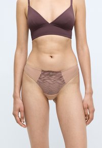 Nude thong with lace accents, featuring a wavy pattern in bronze, and soft fabric. Includes a small metallic logo at the front waistband.