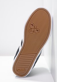 Black textile sneaker with white accents, featuring a textured rubber sole with a herringbone pattern and a tan rubber logo detail.