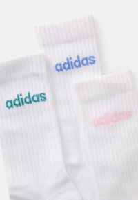 Vita strumpor med ribbad textur, med varumärkesnamnet "adidas" i turkos, ljusblå och rosa bokstäver.