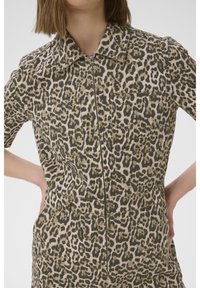Leopard-print zip-up jumpsuit with short sleeves, two chest pockets, and tailored fit. Material appears textured with a smooth finish.
