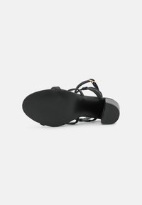 Sandal de salto alto em preto, com tiras finas, sola texturizada e salto quadrado. A parte de baixo tem um acabamento suave com tração em ranhuras.