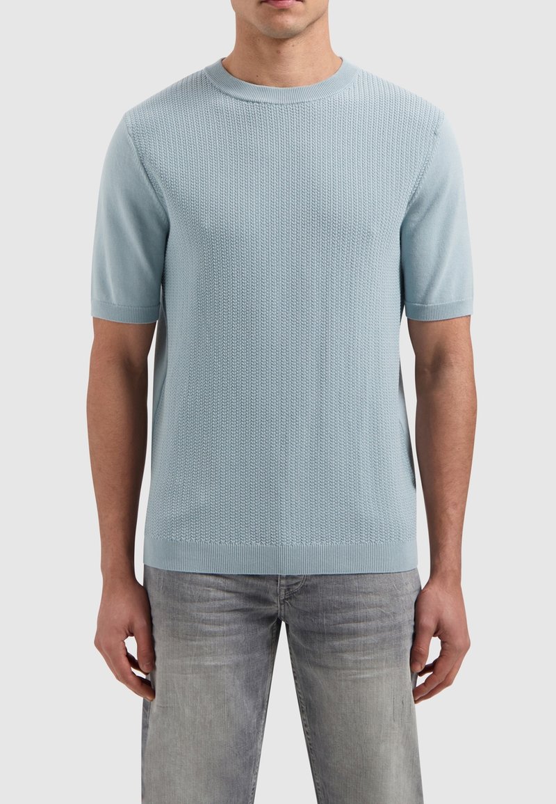 Lichtblauwe gebreide trui met korte mouwen, voorzien van een textuurpatroon, geribbelde kraag en zoom, en een rechte snit. G gedragen met lichtgrijze jeans.