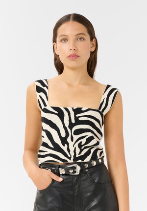 Top in stampa zebro nera e crema con scollatura quadrata e spalline larghe, abbinato a pantaloni in pelle nera a vita alta e una cintura.