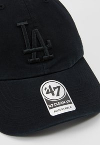 Gorra de béisbol negra hecha de algodón, con un logotipo bordado de "LA" en un color a juego y una correa ajustable en la parte posterior.