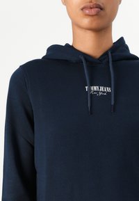 Sweat à capuche bleu marine avec cordons de serrage et un patch logo portant l'inscription "TOMMY JEANS New York" sur la poitrine. Tissu doux.