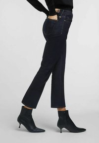 Jeans in denim blu scuro con taglio dritto, dotati di tasche anteriori e posteriori, abbinati a stivali alla caviglia neri con punta appuntita e chiusura con zip.