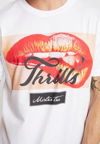 Wit katoenen T-shirt met een grote afbeelding van rode lippen en witte tanden onder de tekst "Thrills" en een merklabel van "Mister Tee".