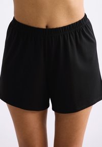 Zwarte korte broek met elastische tailleband, gemaakt van zachte stof. Losse pasvorm met een gladde textuur en zonder zichtbare patronen of metalen details.