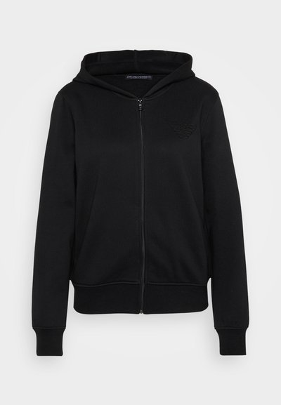 Črna zip-up kapuca s kapuco, ki ima rebraste manšete in rob. Diskretno reliefno logotip se nahaja na levi strani prsnega koša.
