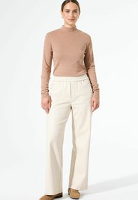 Beige Langarmoberteil mit hohem Kragen, kombiniert mit cremefarbenen, weit geschnittenen Hosen mit elastischem Bund. Glatte Textur über die gesamte Fläche.