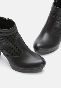 Black ankle boots made of textured synthetic leather, featuring mesh paneling, a curved toe, and a low block heel. Zipper closure at the back.