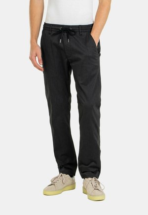 Schwarze, lässige Hosen mit elastischem Bündchen und Kordelzug; zwei Seitentaschen; getragen mit hellen Sneakers. Glatte Stoffoberfläche.