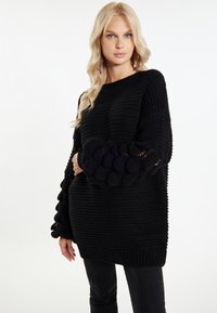 Maglione nero lavorato a maglia con una vestibilità comoda, un motivo a coste testurizzato e dettagli delle maniche a sbuffo. Accentuato da un motivo di lavorazione a maglia a contrasto ai polsini.