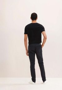 Maglietta nera a maniche corte, aderente. Pantaloni scuri con taglio slim. Scarpe da ginnastica bianche. Design semplice, senza motivi né elementi visibili.