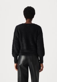 Czarny puszysty sweter z długimi, balonowymi rękawami i szerokim dekoltem, w połączeniu z dopasowanymi czarnymi skórzanymi spodniami. Tekstura wydaje się miękka i puszysta.