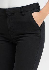 Melni kokvilnas maisījuma bikses ar gludu tekstūru, šauru piegriezumu un sānu kabatām. Iekļauj klasisku jostasvietu ar jostas cilpiņām un minimāliem šuves detaļām.