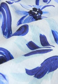 Bomuldsstof med blå blomster mønstre på en lys baggrund, der har flydende penselstræk design og blød tekstur.