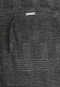 Tissu noir et blanc en tartan de Calvin Klein avec un tissage texturé. Présente une petite étiquette en métal argenté. Motif distinctif et contraste de couleurs.