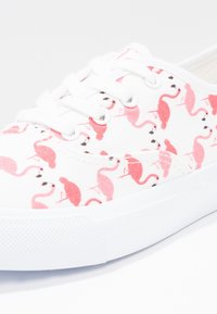 Baskets en toile blanches avec un motif de flamant rose, dotées de lacets blancs et d'une semelle en caoutchouc texturé. Les accents comprennent des détails noirs pour les yeux.