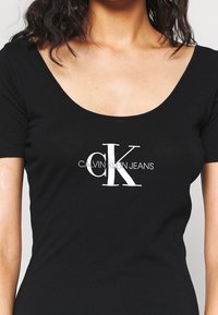 Černý krátký rukáv tričko z bavlny s kulatým výstřihem, na přední straně se středem bílým logem "CK" a textem "CALVIN KLEIN JEANS".