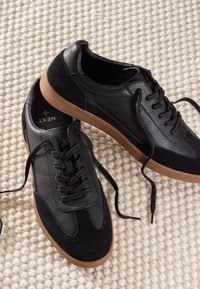 Črni športni copati iz teksturirane usnjene in semišane kože, s podplatom iz gumijaste gume, zaobljenim noskom, ravnimi vezalkami in majhnim logotipom.