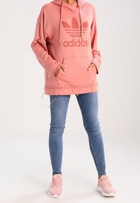 Růžová oversized mikina s velkým tonálním logem Adidas, spárovaná se světle modrými skinny džíny a růžovými sportovními botami s texturovanou tkaninou.