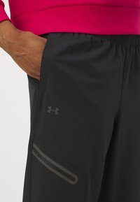 Mustat urheilushortsit, joissa on joustava vyötärö, sivutasku vetoketjulla ja huomaamaton Under Armour -logo tummanharmaana. Valmistettu sileästä, kevyestä materiaalista.