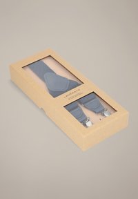 Niebieskie szelki zaprezentowane w przezroczystym pudełku z zewnętrzną warstwą z papieru kraft, z srebrnymi elementami i trójkątnym wzorem na paskach.