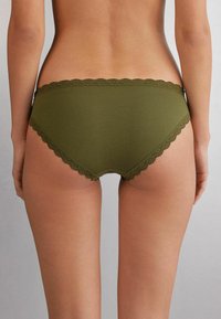 Olijfgroene katoenen bikini slipjes met geschulpte kanten rand langs de taille en beenopeningen, een gladde textuur en een medium hoge pasvorm.