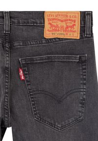 Svarta jeans i denim med en läderetikett med röda och orangea grafikdetaljer. Märkbar röd flik på bakfickan och signaturstygn.