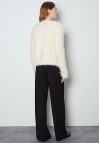 Maglione bianco e morbido con maniche lunghe, caratterizzato da una finitura testurizzata. Abbinato a pantaloni neri a gamba larga, visto da dietro.